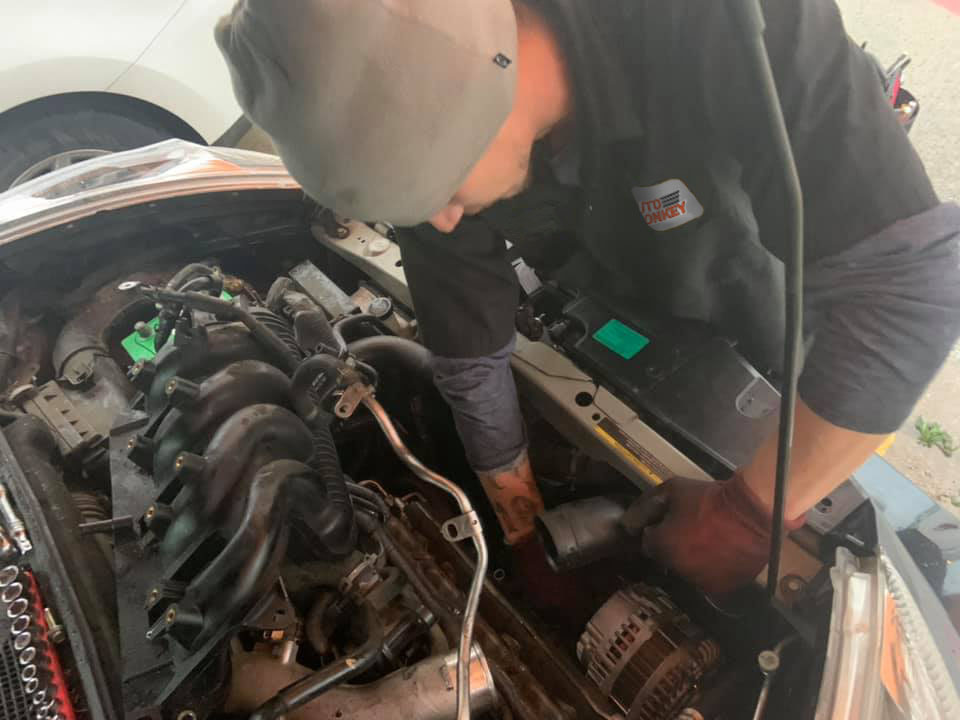 mobile mechanic working on alternator and removing exhaust manifold